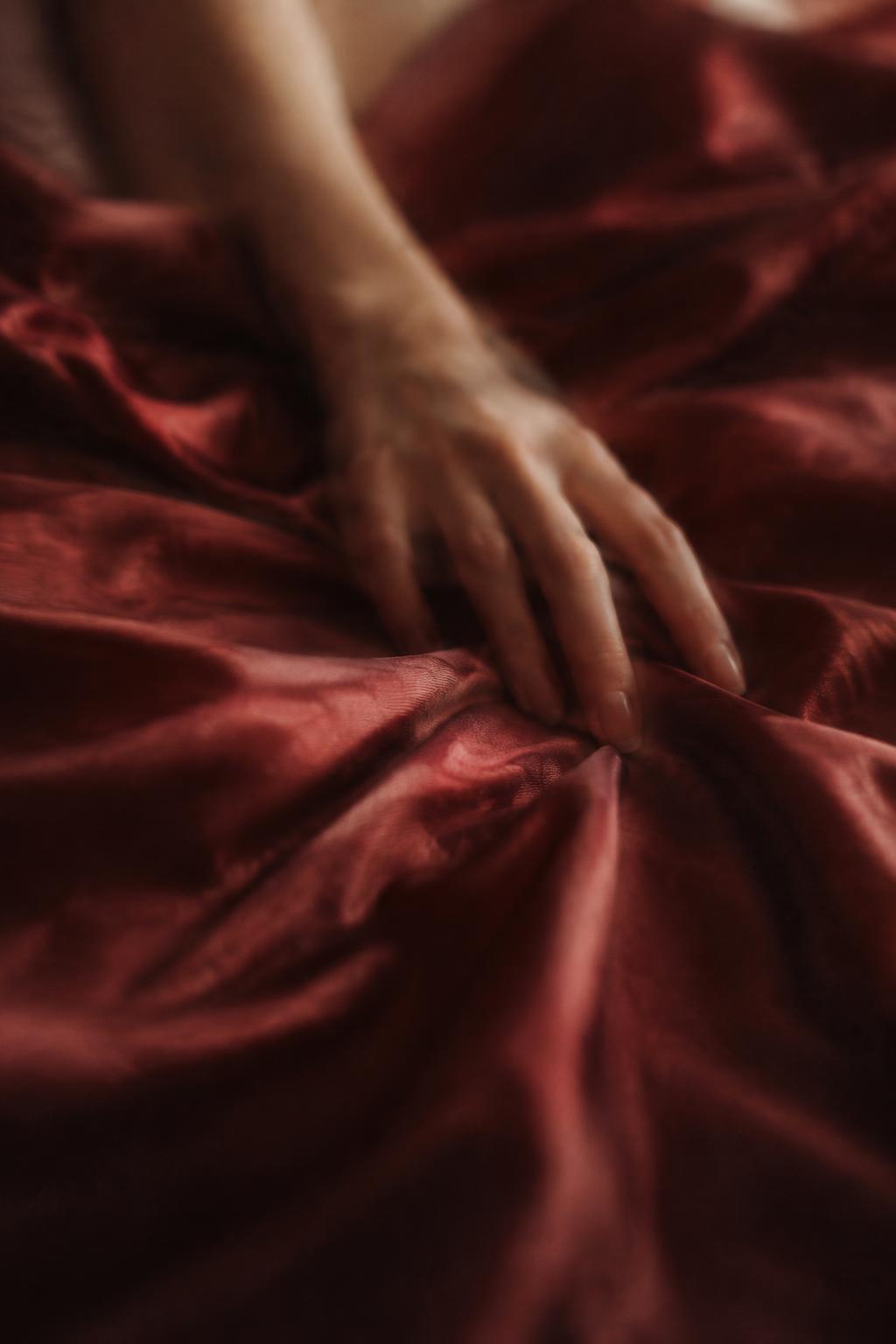a relaxed hand resting on deep red silk sheets